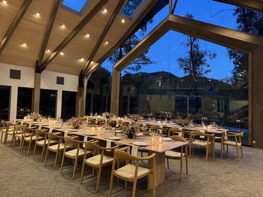 Long candlelit dinner table set up under a glass-walled event hall